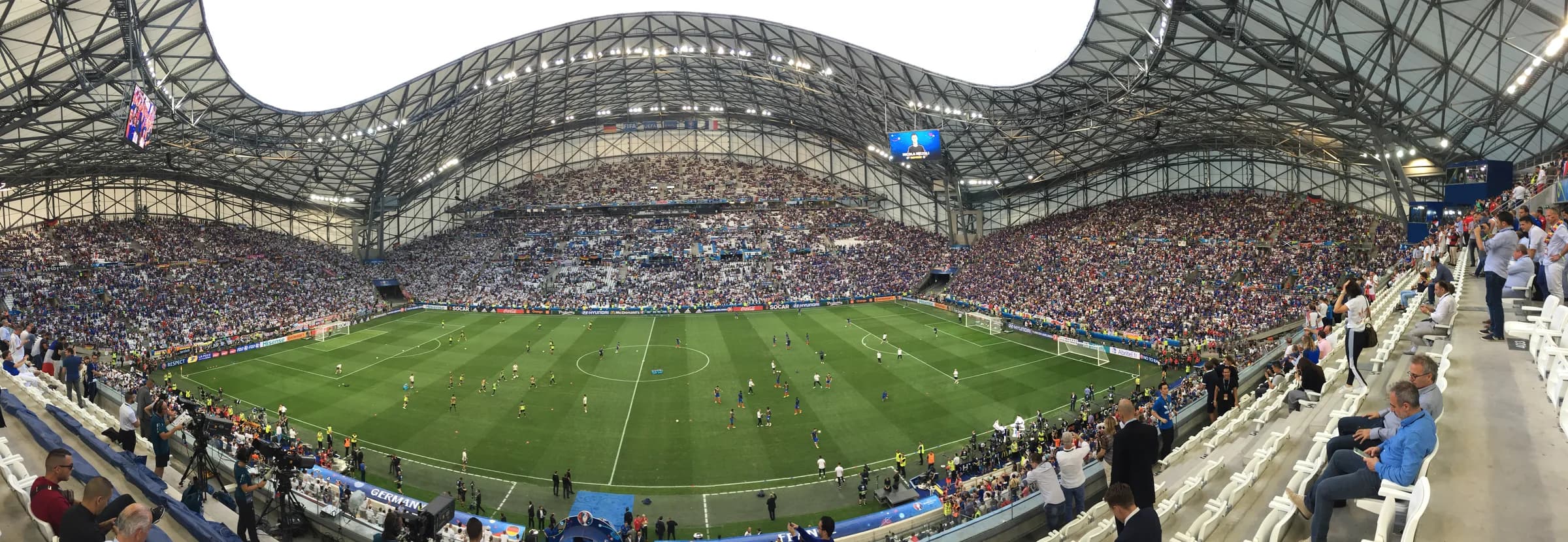 Vue intérieure du Stade Vélodrome de Marseille, avec sa pelouse et sa toiture ondulée.